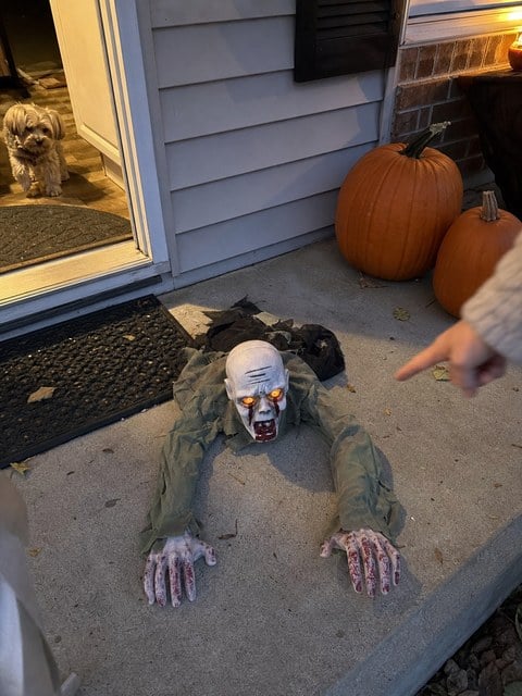 Crawling zombie decoration beside a porch doormat and pumpkins