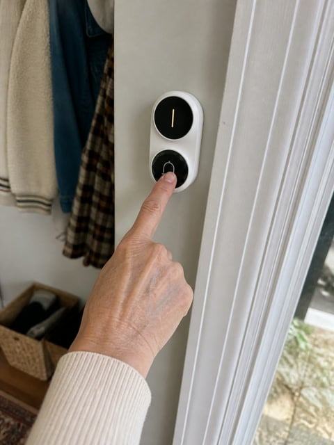 A homeowner pressing a white wireless doorbell button beside the entry door