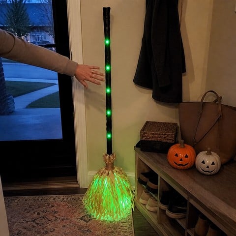 A hand activating the glowing witch broom in an entryway