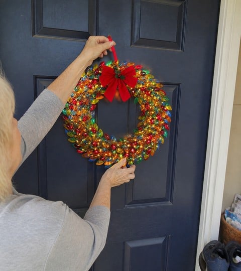 Colorful lighted wreath being hung on a navy front door